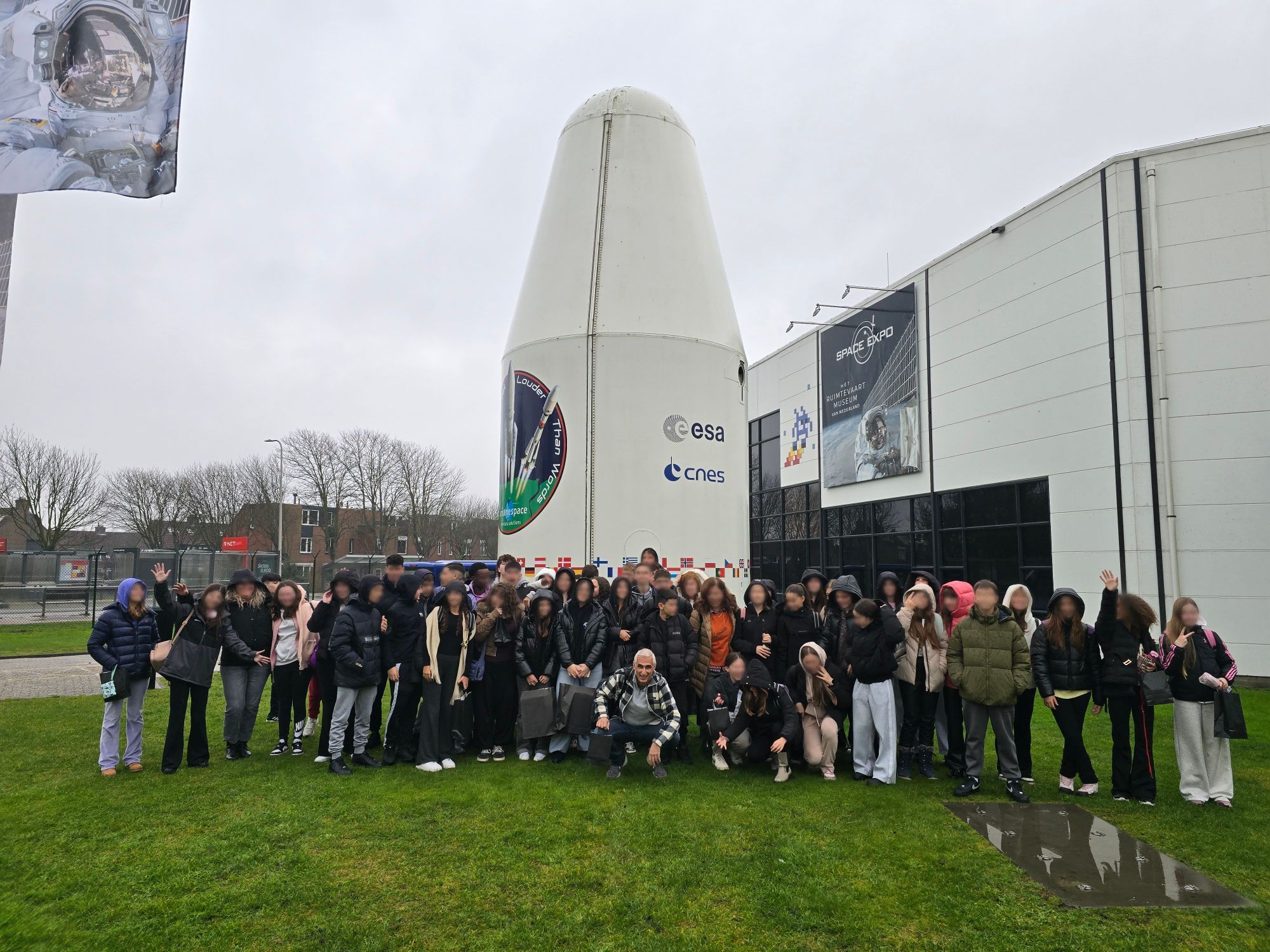 A school group with their guide outside Space Expo in Noordwijk, beside a full-size rocket nose cone.