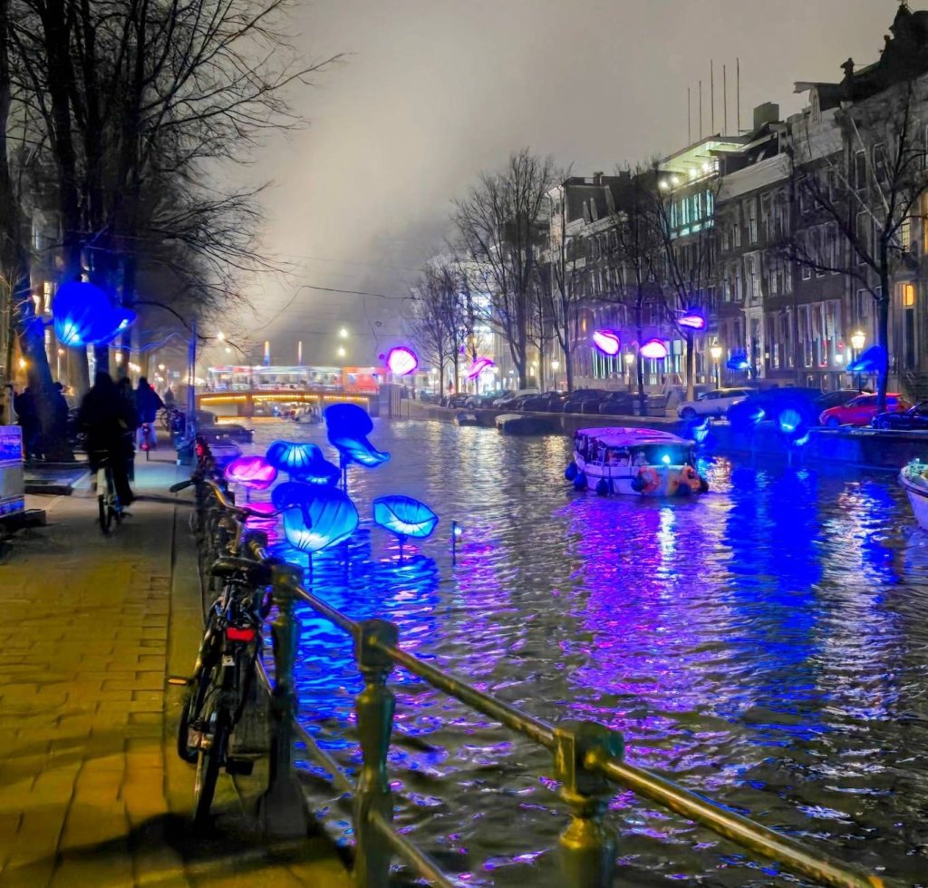 Φωτεινές εγκαταστάσεις του Amsterdam Light Festival πάνω στο νερό ενός καναλιού του Άμστερνταμ, με τα φώτα να καθρεφτίζονται