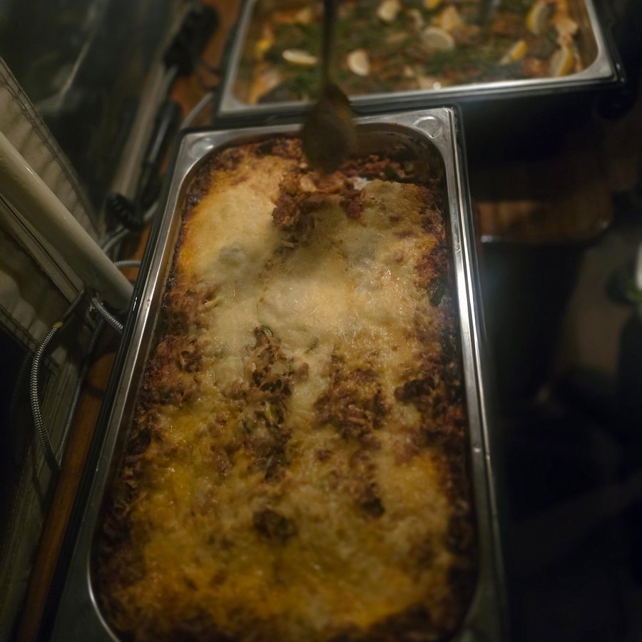 Lasagne with a golden cheese crust in a steel tray on the Italian buffet aboard a canal boat, a long spoon serving a portion