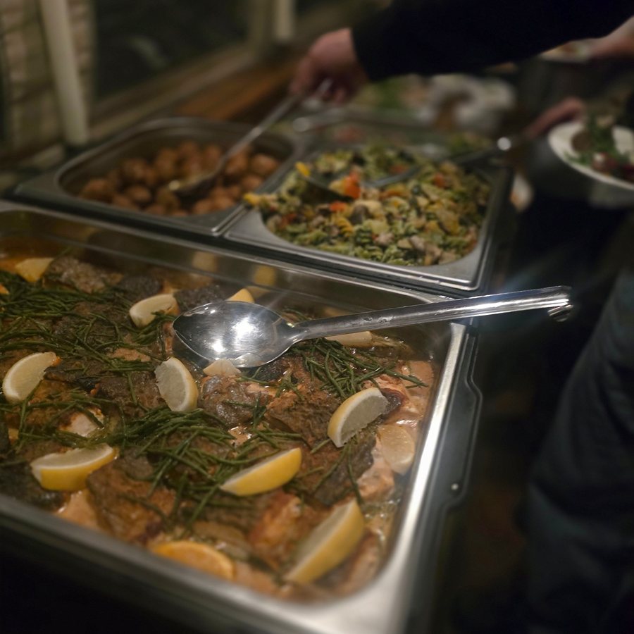 Roasted salmon fillets topped with samphire and lemon wedges in a steel tray on the Italian buffet aboard a canal boat, a guest serving themselves